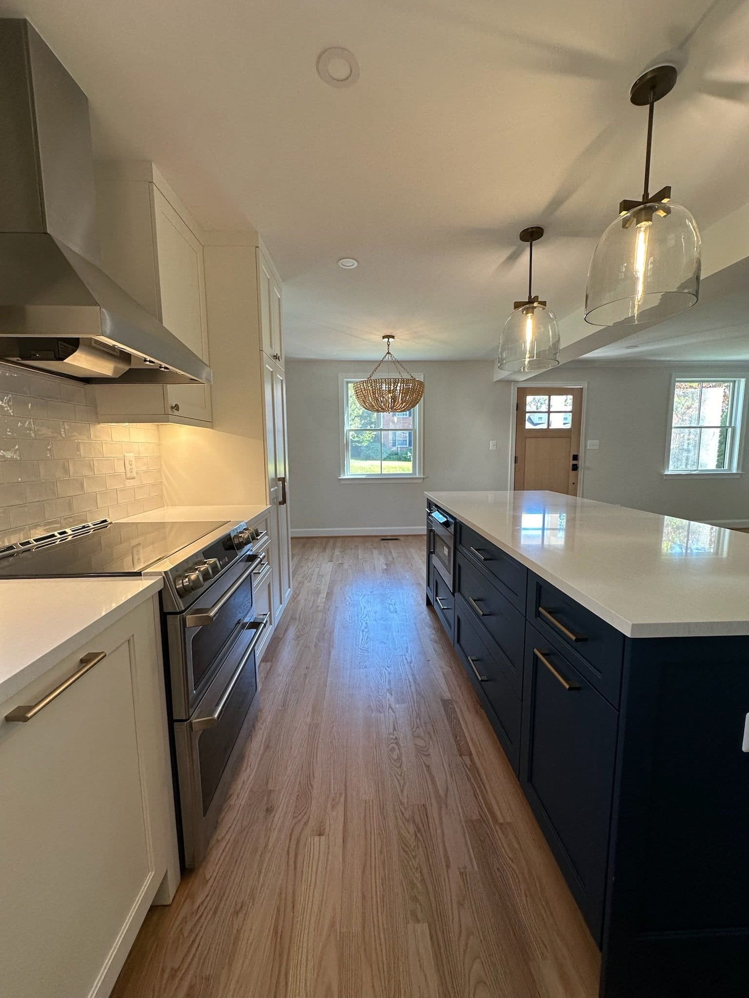 Long kitchen with white cabinets, a navy island and hardwood floors